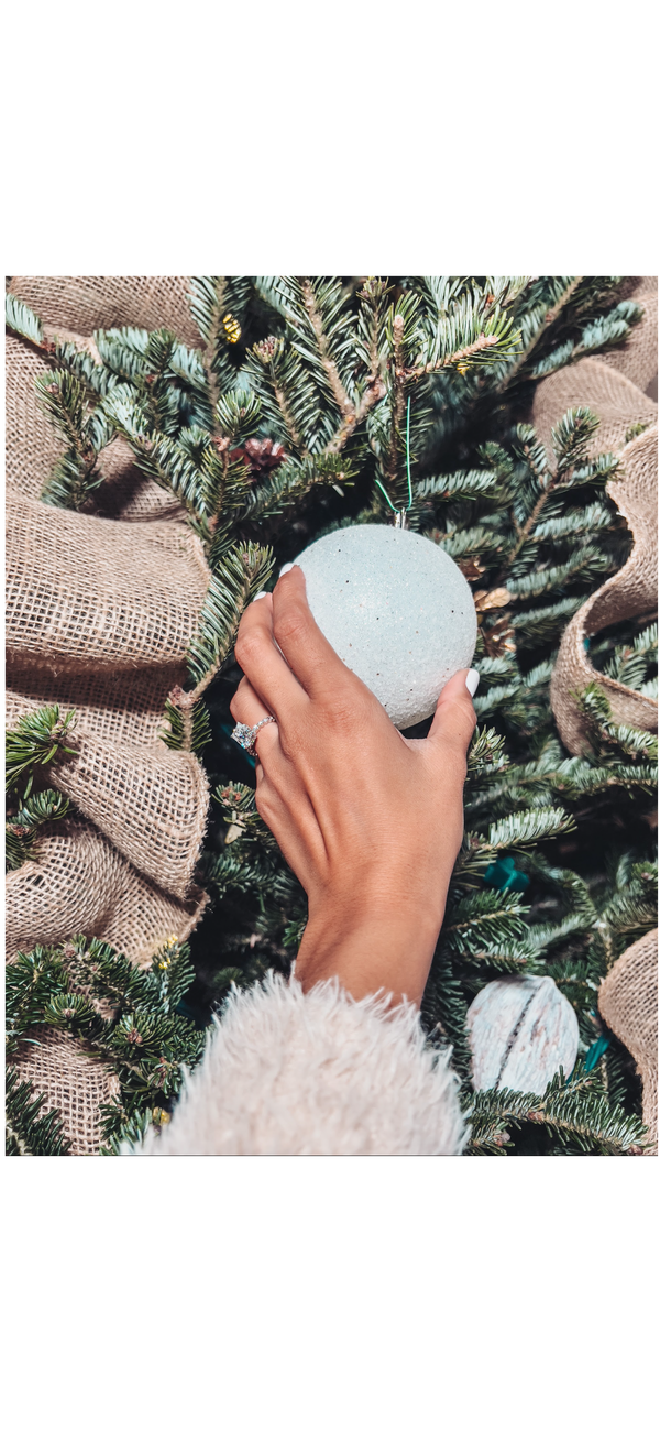 Closeup of hand with Moissanite engagement ring putting an ornament on tree