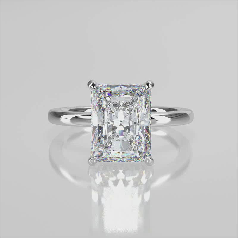 Elongated radiant cut centre stone with rounded plain band. Accent diamond gallery and non-cathedral setting. 